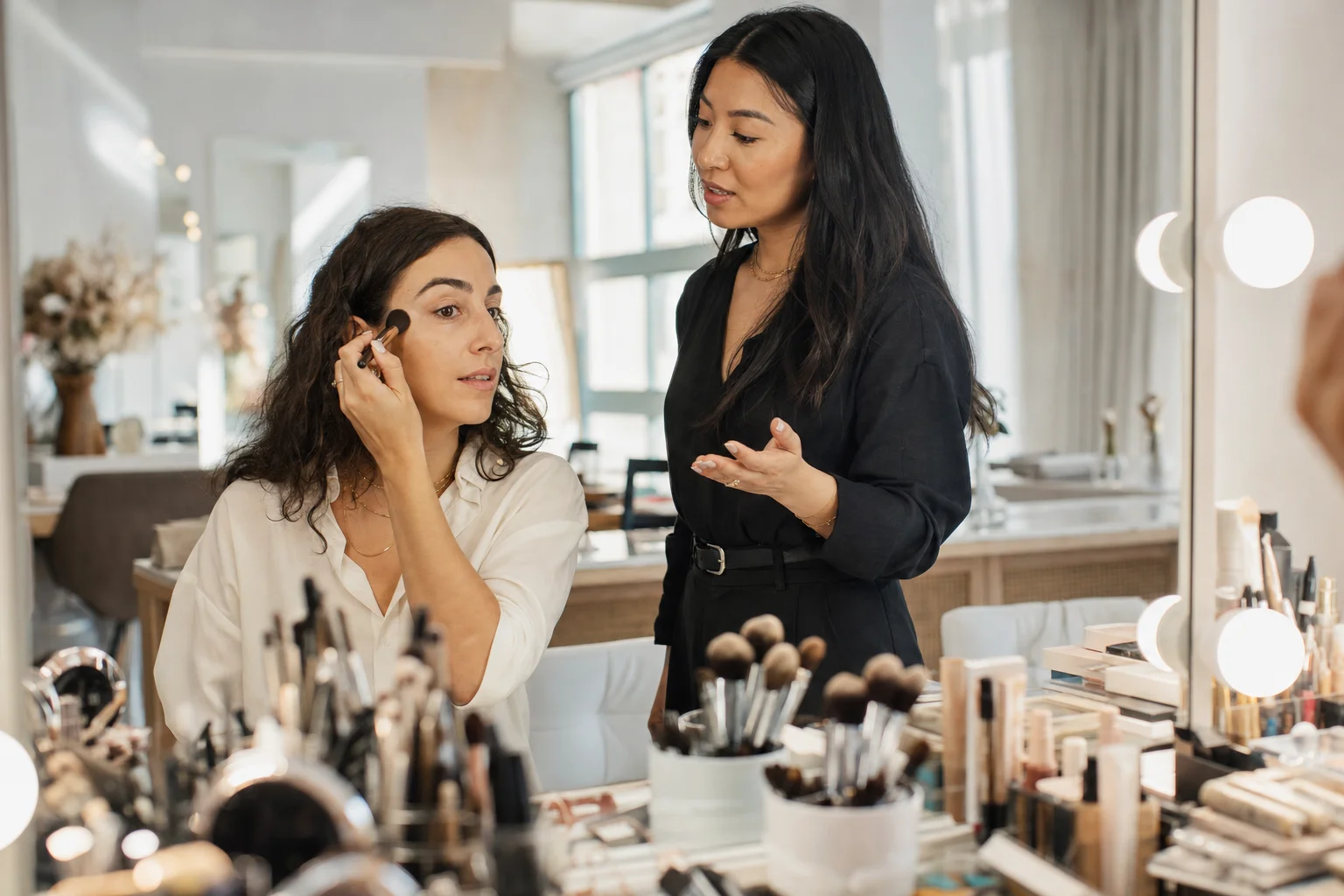 Artist guiding a client applying her own makeup during a lesson